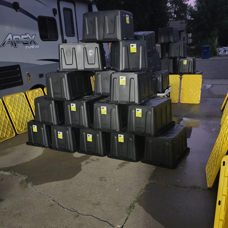A pyramid of moving totes drying at dusk with yellow lids lined up along the driveway