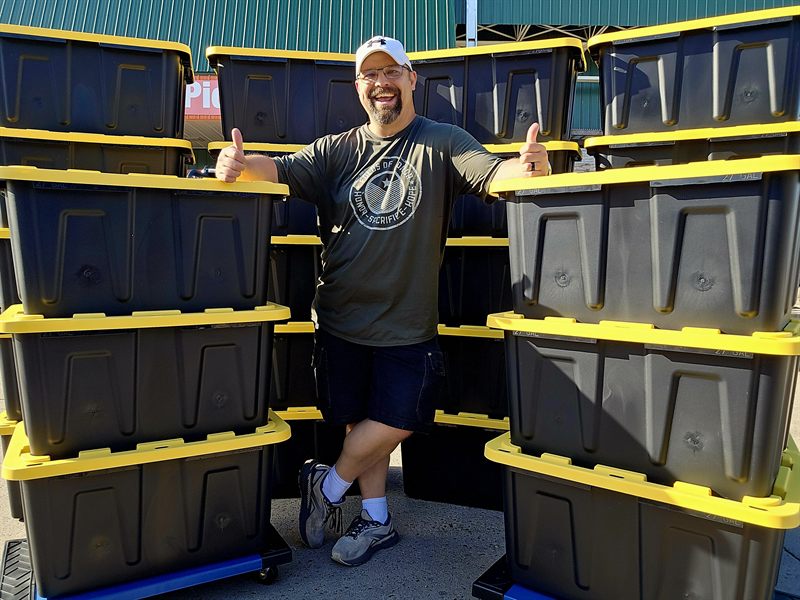 Tori of TNT Rental giving two thumbs up between tall stacks of black and yellow moving totes