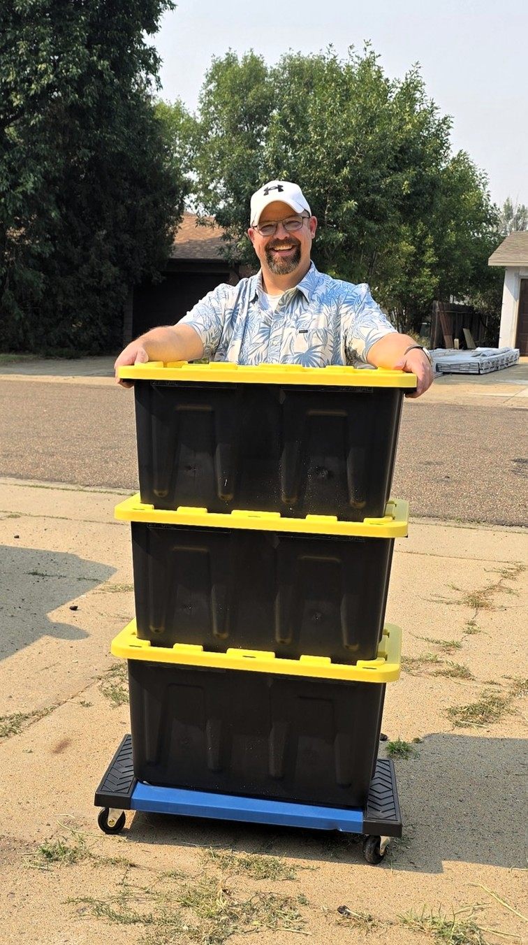 Tori of TNT Rental smiling behind three stacked moving totes on a rolling Tote Cart