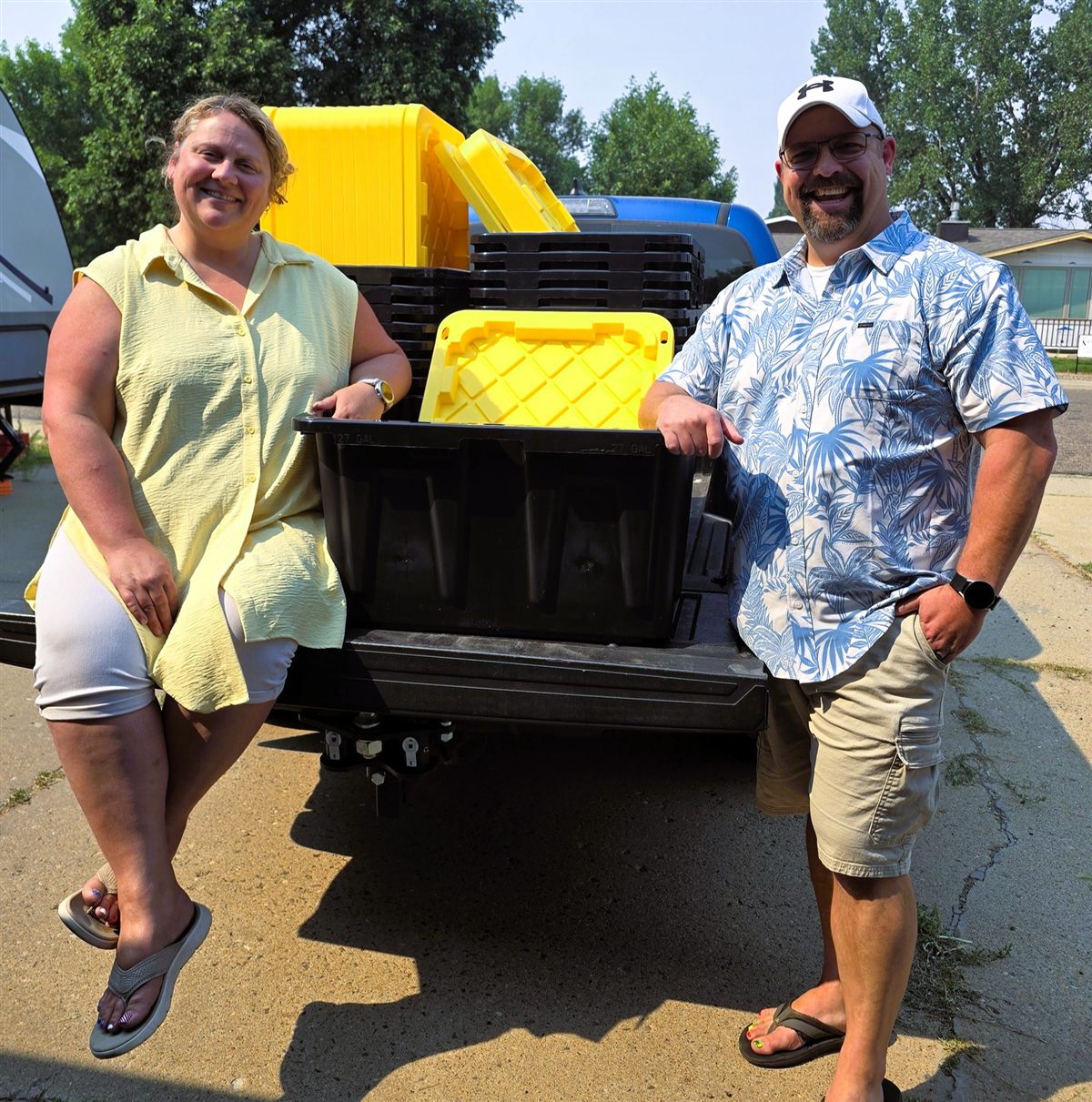 Traci and Tori of TNT Rental smiling at the tailgate of their truck loaded with black and yellow moving totes